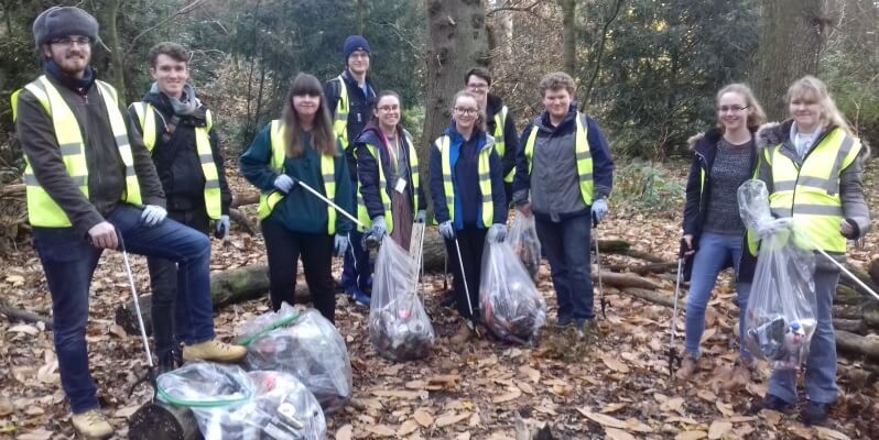 Group of students wearing hi-vis jackets and carrying bags of collected litter